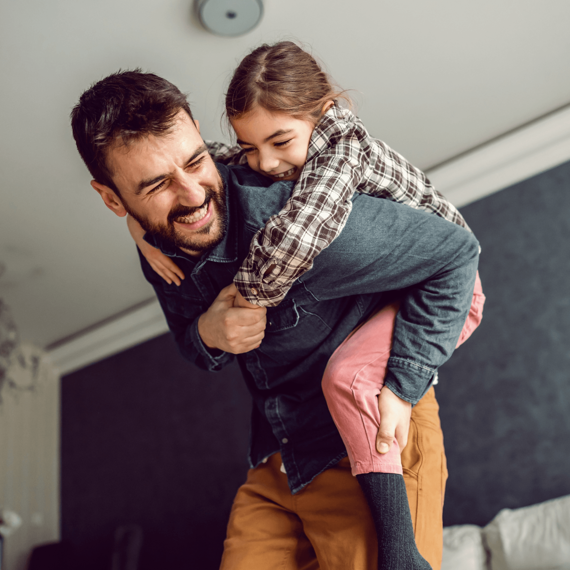 Père portant sa fille sur son dos riant ensemble intérieur chaleureux