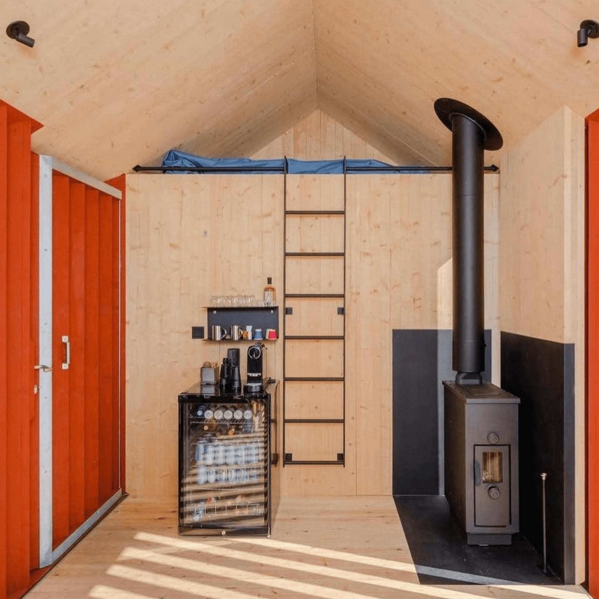 Intérieur fonctionnel d’un refuge flottant scandinave avec poêle à bois et cuisine équipée.
