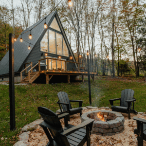 Cabane triangulaire noire avec grandes baies vitrées feu de camp et guirlandes lumineuses