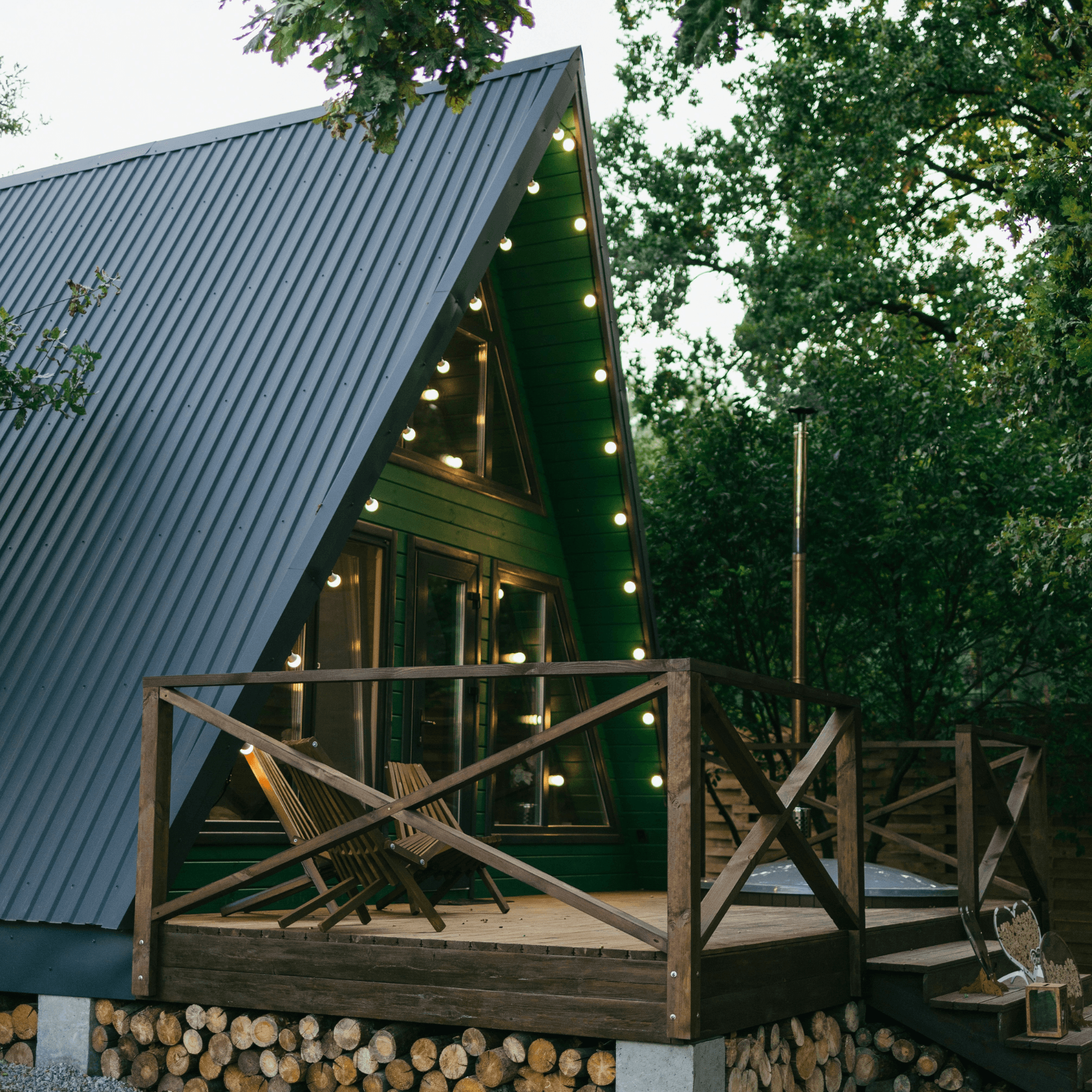 Terrasse bois cabane verte triangulaire guirlandes lumineuses chaises longues forêt