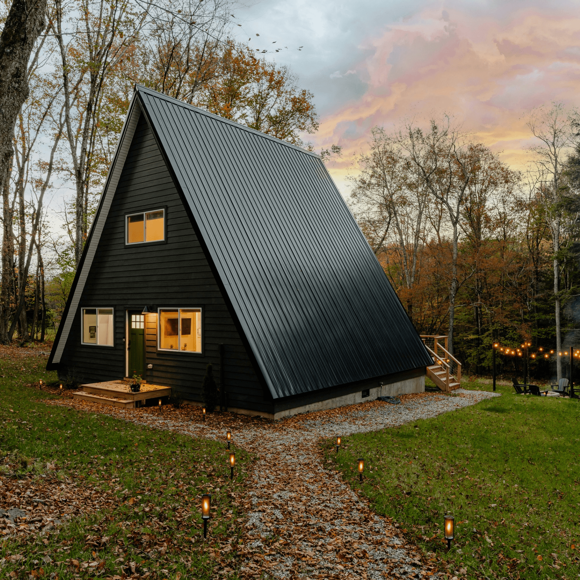 Cabane noire triangulaire éclairée crépuscule rose forêt automne allée gravier