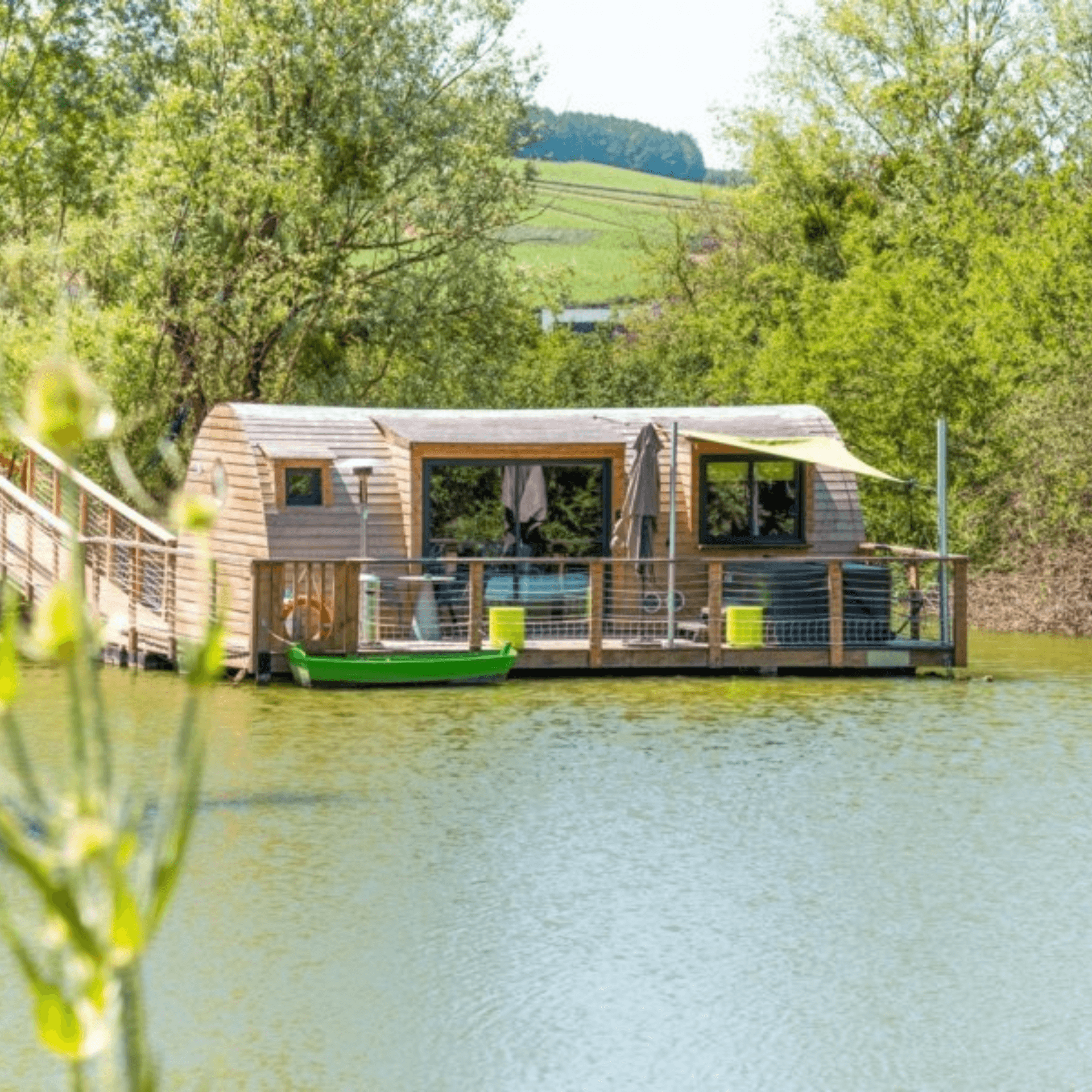 Cabane flottante bois forme arrondie terrasse étang roseaux verts reflets eau