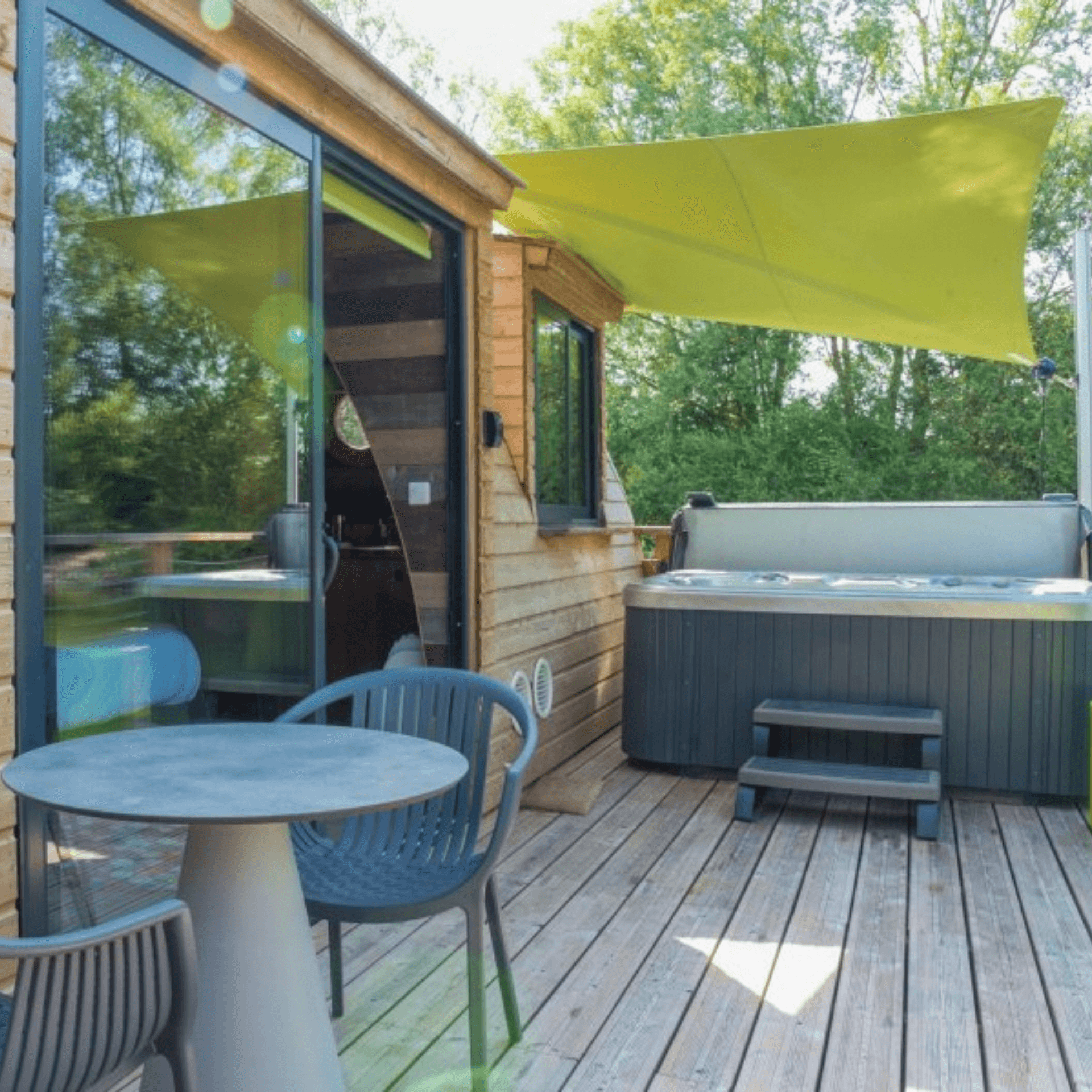 Terrasse bois jacuzzi extérieur table chaises bleues voile ombrage vert cabane flottante